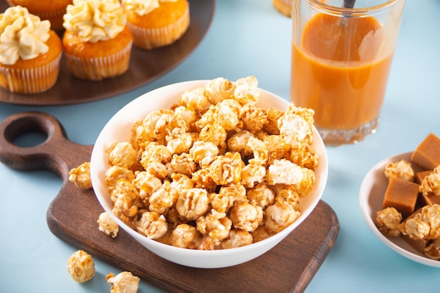 Caramel popcorn snack on white bowl with delicious cupcakes and caramel syrup in jar on the background