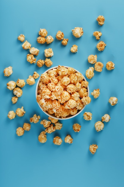 Caramel popcorn in a white glass cup with scissors on a blue background. A delicious catch for filming movies, TV series, cartoons. Free legal, crimes.