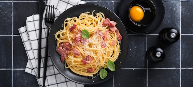 Carbonara pasta Spaghetti with pancetta egg parmesan cheese and cream sauce on old black tile table background Traditional italian cuisine and dish Pasta alla carbonara Top view