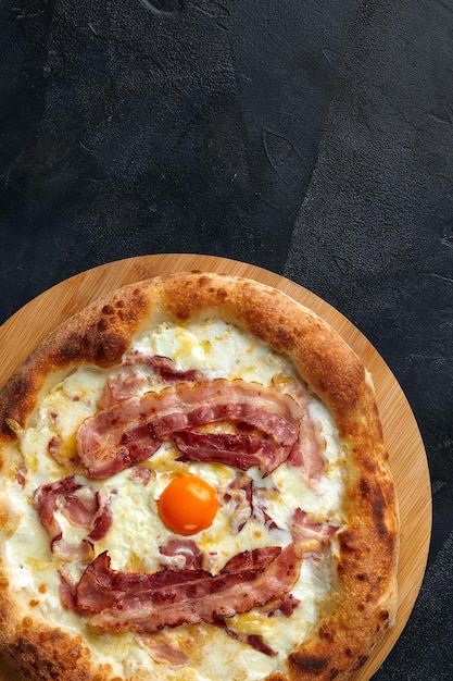 Carbonara pizza with bacon and egg on dark stone background