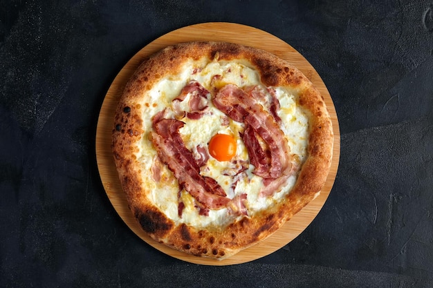 Carbonara pizza with bacon and egg on dark stone background