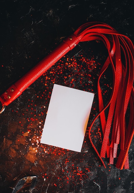 card mockup, mockup of a white sheet of paper bdsm toys, red leather whip on a black background with