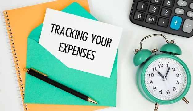 Card on a postal envelope with the text TRACKING YOUR EXPENSES, clock, calculator, pen.