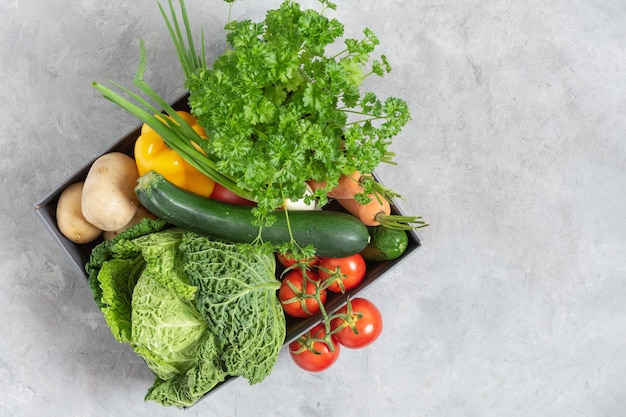 Cardboard box full of fresh organic vegetables from the local market on grey table