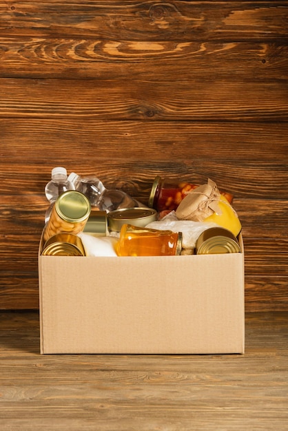 Cardboard box with donated food on wooden background charity concept