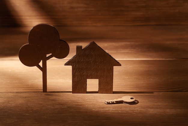 Cardboard cutout house next to a tree and keys on a wooden background Home purchase mortgage