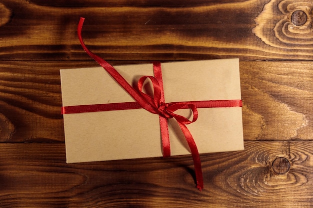 Cardboard gift box with red ribbon on wooden table. Top view