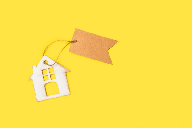 A cardboard house with a brown blank paper label on a yellow background with copy space