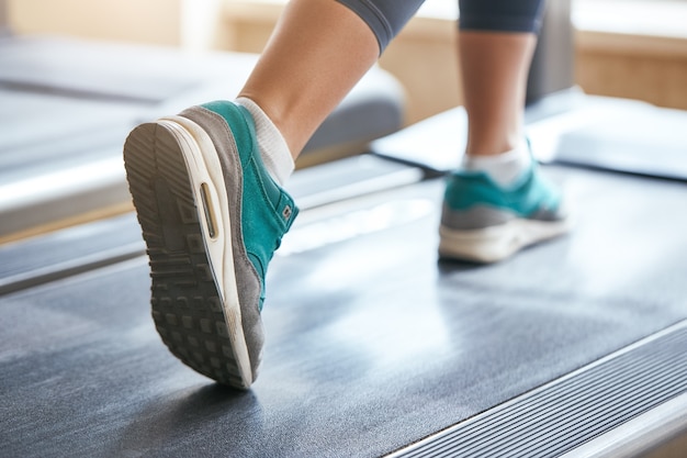 Cardio workout cropped photo of woman in sports shoes running on treadmill at gym