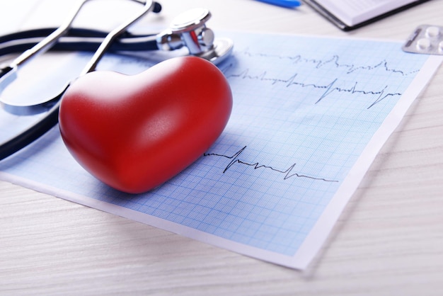 Cardiogram with stethoscope and red heart on table closeup