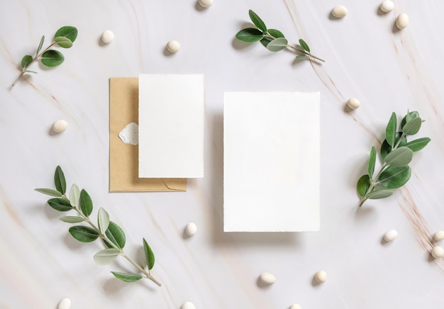 Cards and envelope on a marble table near eucalyptus branches and pebbles top view Wedding mockup