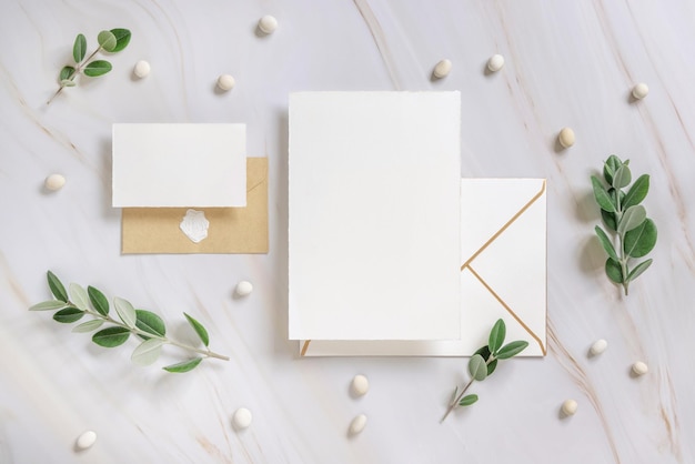 Cards and envelope on a marble table near eucalyptus branches and pebbles top view Wedding mockup