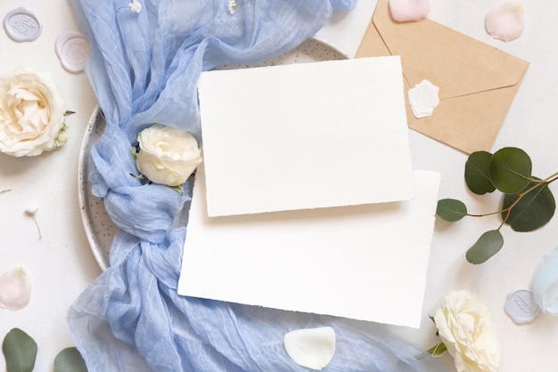 Cards near light blue tulle fabric knot and cream roses on plates top view copy space wedding mockup