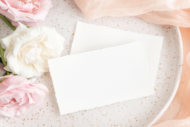 Cards near light pink tulle fabric and roses on plate top view copy space wedding mockup