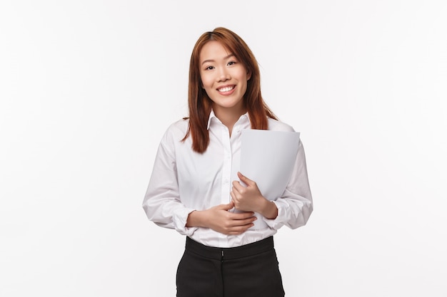 Career, profession and women concept. Friendly-looking elegant young office lady want help customer, smiling pleasant camera holding documents near chest, talking to boss or company manager