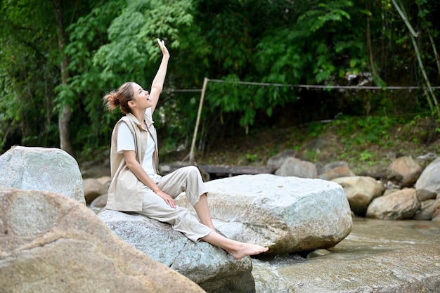 Carefree Asian female sitting near the river on the river stone getting some fresh air Camping