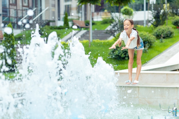 Carefree childhood. Nice happy girl smiling while stretching her hands out to the water