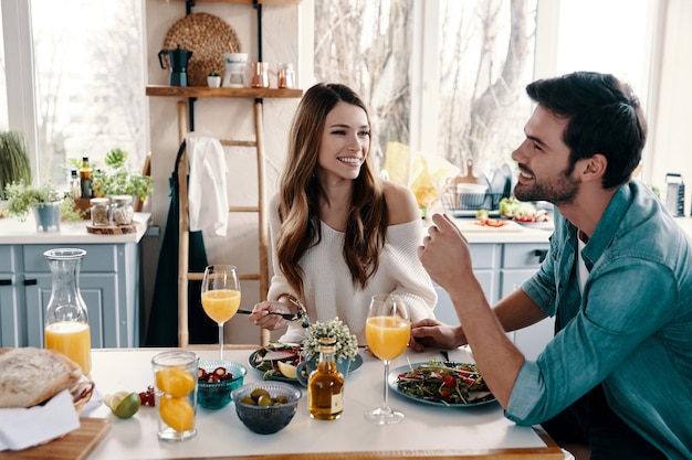 Carefree couple. Beautiful young couple enjoying healthy breakfast while sitting in the kitchen at home