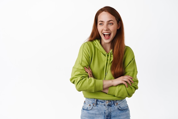 Carefree ginger girl laughing, enjoying happy moments, cross arms and looking amused aside at left copy space, have joyful conversation, white background.