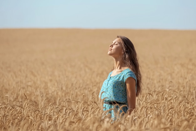 Carefree girl in a blue sundress enjoys the sun in a wheat field