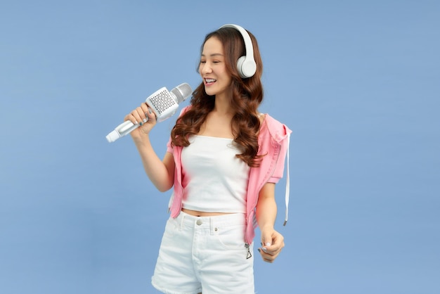 Carefree happy asian woman singing in microphone listen music in headphones blue background