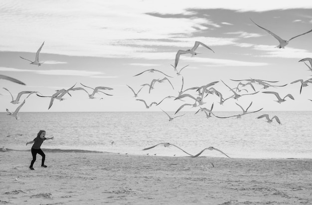 Photo carefree kid running chasing birds kid runs along the coast and chases the birds seagull fly away boy and seagull on the beach excited boy running on the beach