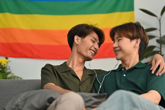 Carefree male gay couple listening to music on earphones spending time together at home LGBT relationship and comfort living concept