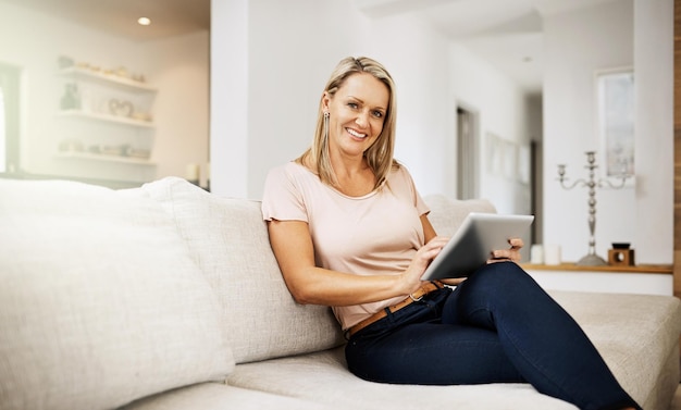 Carefree and relaxed woman browsing on a tablet enjoying her weekend and sitting on the sofa at home Portrait of a mature comfortable happy female surfing the internet in the living room