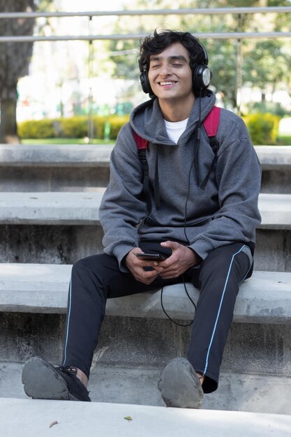 Carefree teenager listening to music with headphones in park, smiling and relaxed