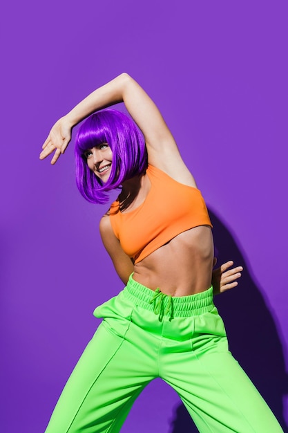 Carefree woman dancer wearing colorful sportswear having fun against purple background