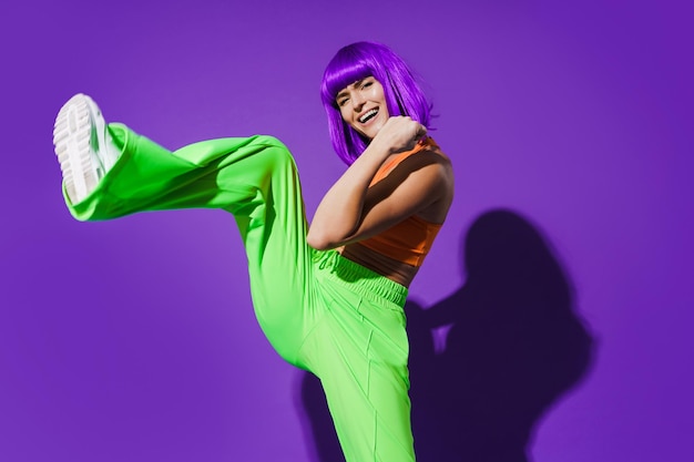 Carefree woman dancer wearing colorful sportswear having fun against purple background