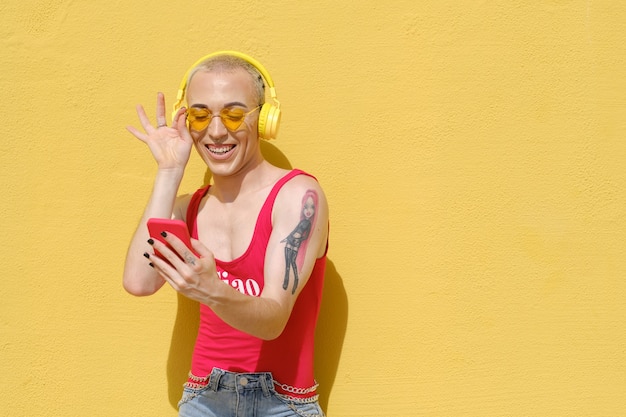 Carefree young non-binary person smiling while enjoying listening to music with a mobile phone and wireless headphones.