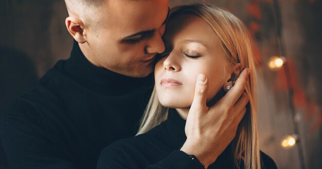 Careful caucasian man embracing his blonde wife and trying to kiss her touching her face