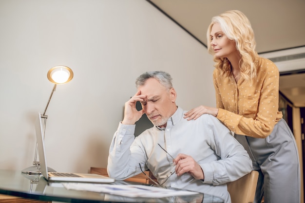 Careful wife. A man working from home and feeling tired, his wife supporting him