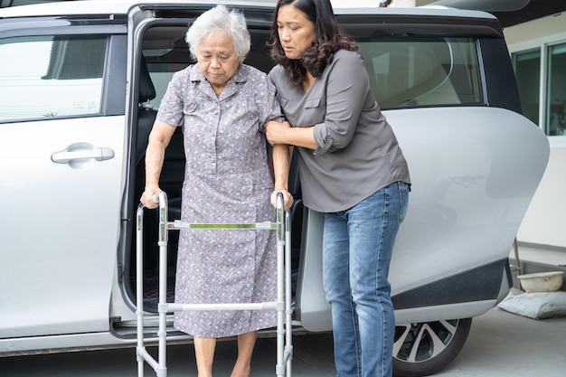 Caregiver daughter help and support asian senior or elderly old lady woman patient prepare get out her car.