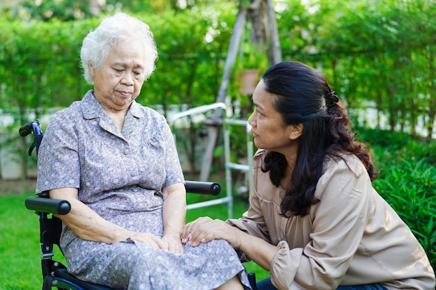 Caregiver help Asian elderly woman disability patient sitting on wheelchair in park medical concept