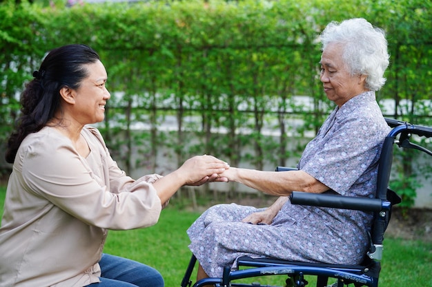 Caregiver help Asian elderly woman disability patient sitting on wheelchair in park medical concept