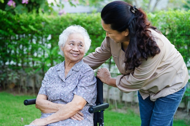 Caregiver help Asian elderly woman disability patient sitting on wheelchair in park medical concept