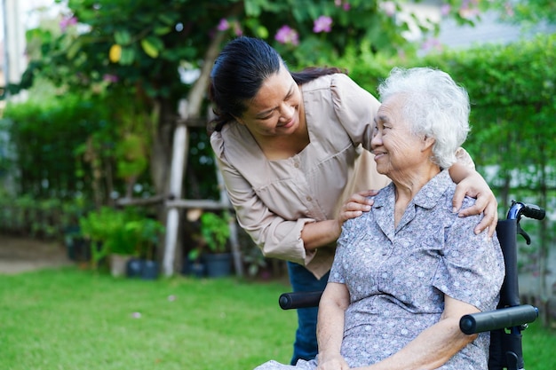 Caregiver help Asian elderly woman disability patient sitting on wheelchair in park medical concept