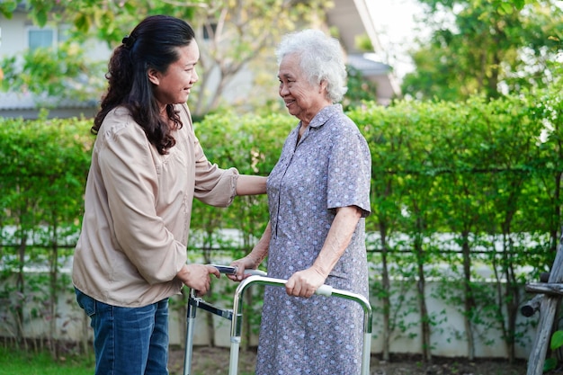 Caregiver help Asian elderly woman disability patient walk with walker in nursing hospital medical concept