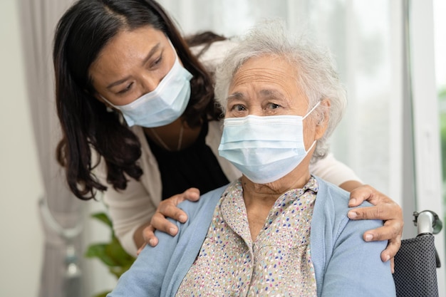 Caregiver help Asian senior or elderly old lady woman sitting on wheelchair and wearing a face mask for protect safety infection Covid19 Coronavirus