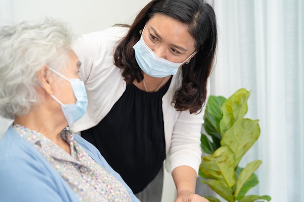 Caregiver help Asian senior or elderly old lady woman sitting on wheelchair and wearing a face mask for protect safety infection Covid19 Coronavirus