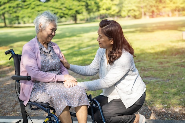 Caregiver help and care Asian senior or elderly old lady woman patient sitting and happy on wheelchair in park healthy strong medical concept