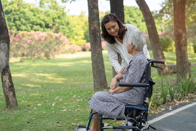 Caregiver help and care Asian senior or elderly old lady woman patient sitting and happy on wheelchair in park healthy strong medical concept