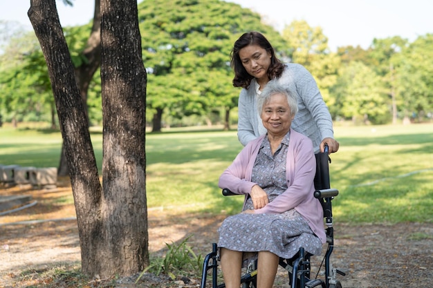 Caregiver help and care Asian senior or elderly old lady woman patient sitting and happy on wheelchair in park healthy strong medical concept