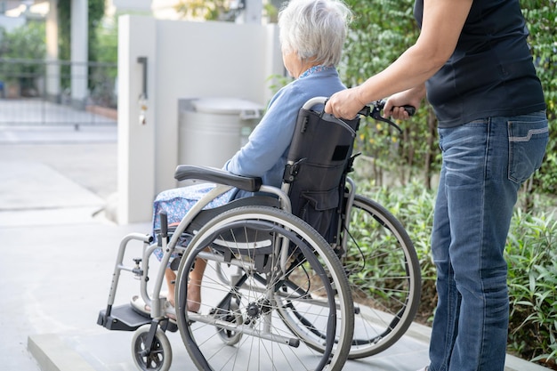 Caregiver help and care Asian senior or elderly old lady woman patient sitting on wheelchair at nursing hospital ward healthy strong medical concept