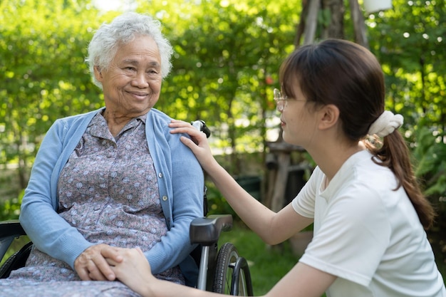 Caregiver help and care Asian senior or elderly old lady woman patient sitting on wheelchair in park healthy strong medical concept