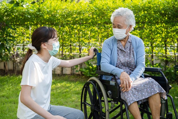 Caregiver help and care Asian senior or elderly old lady woman patient sitting on wheelchair in park healthy strong medical concept