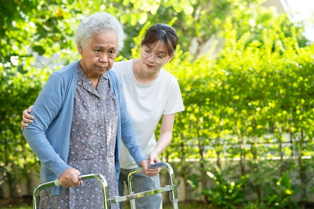 Caregiver help and care Asian senior or elderly old lady woman use walker with strong health while walking at park in happy fresh holiday