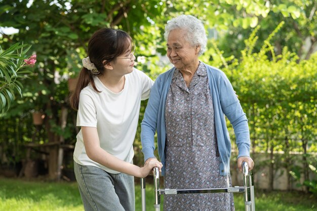 Caregiver help and care Asian senior or elderly old lady woman use walker with strong health while walking at park in happy fresh holiday